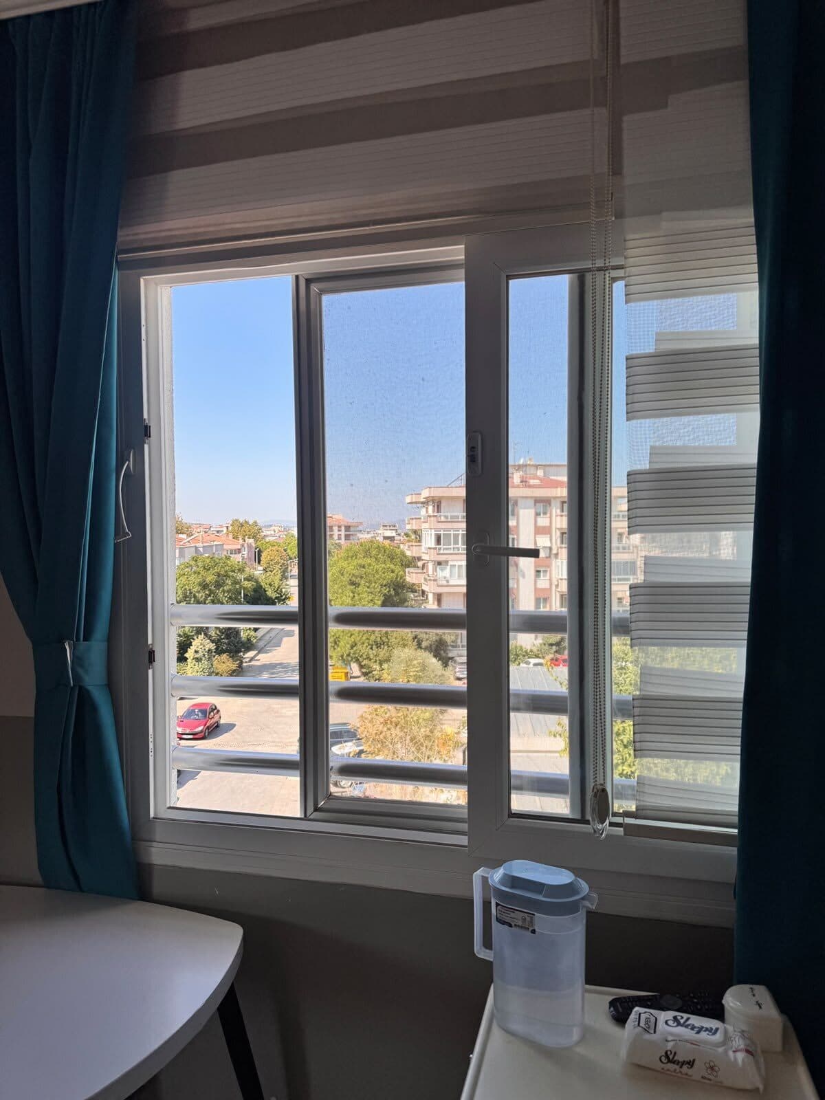 Sakin odasında pencere önü: açık pencere, perde ve masadaki su sürahisi